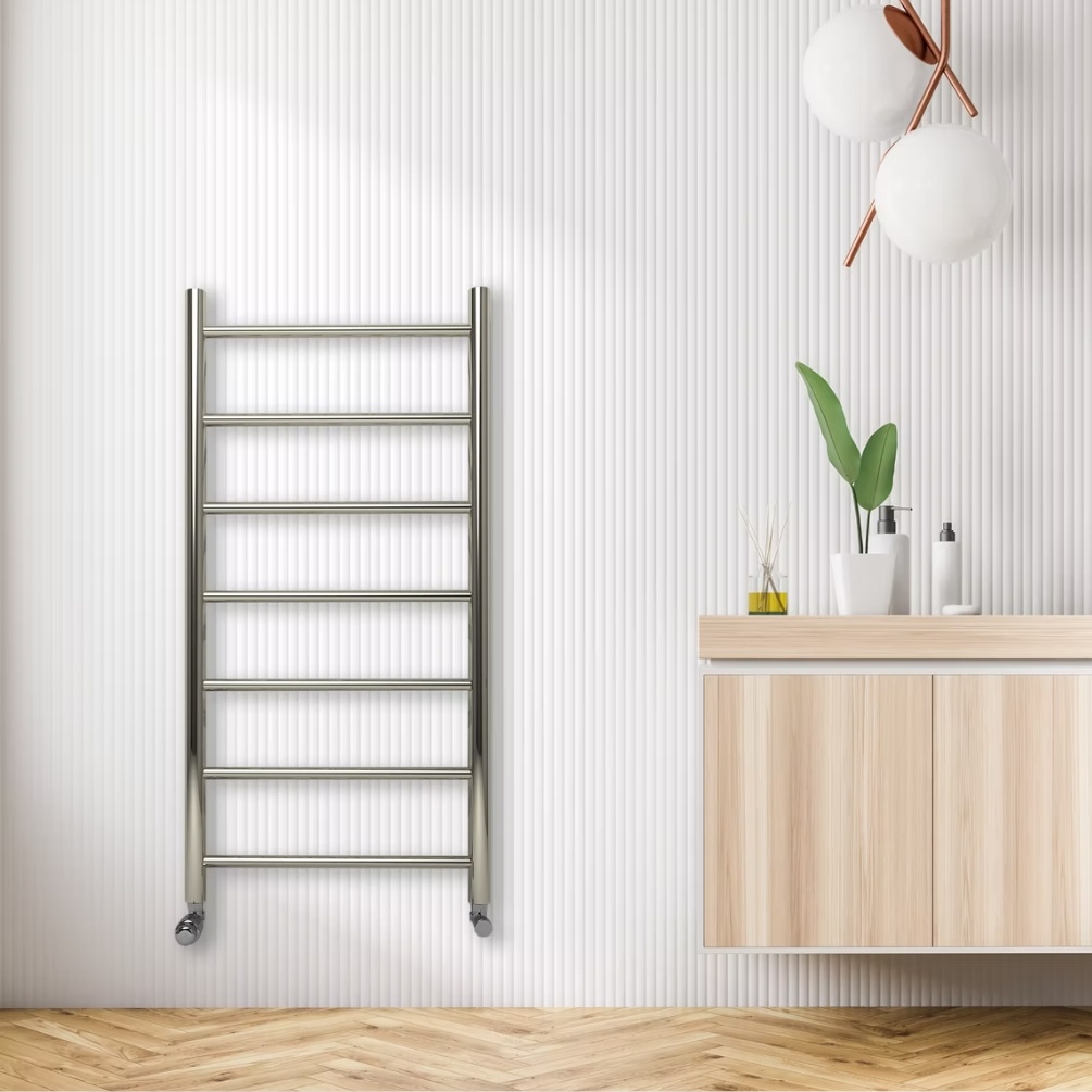 Lifestyle image of the Radox Space 1076mm x 538mm Polished Stainless Steel Heated Towel Rail mounted on a white bathroom wall, next to a large countertop vanity unit